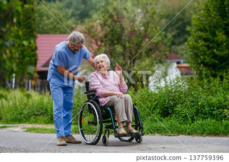 Senior patient and male nurse talking during walk outdoors. Senior patient and male nurse talking during walk outdoors. 137759396