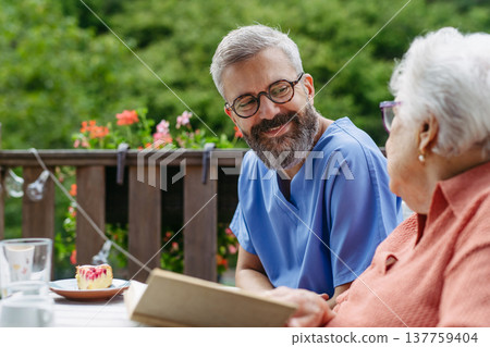 Caregiver spending time with elderly woman, reading book. Caregiver spending time with elderly woman, reading book. 137759404
