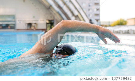 Focused swimmer performing crawl stroke in water. Focused swimmer performing crawl stroke in water. 137759482