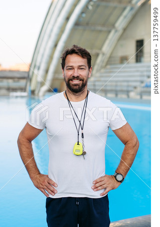 Professional swimming coach standing by outdoor pool. Professional swimming coach standing by outdoor pool. 137759499
