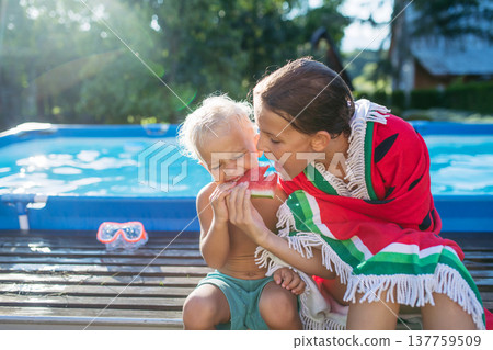 Sister and toddler brother eating watermelon after swimming in pool. 137759509