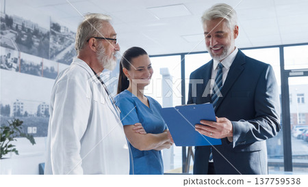 Medical sales representative presenting new medication to doctors, standing hospital hallway. Medical sales representative presenting new medication to doctors, standing hospital hallway. 137759538