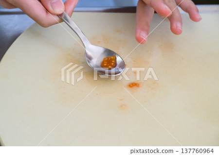 A hand scooping tomato seeds from a cutting board with a spoon. A hand scooping tomato seeds from a cutting board with a spoon. 137760964