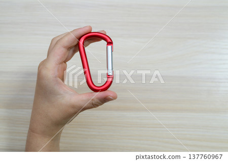 A hand holding a red carabiner against a wood-grain background. 137760967