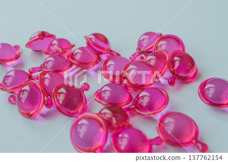 Close-up macro shot of many glossy pink hair treatment capsules. Focused foreground highlights the rich oil and reflective texture Close-up macro shot of many glossy pink hair treatment capsules. Focused foreground highlights the rich oil and reflective texture 137762154