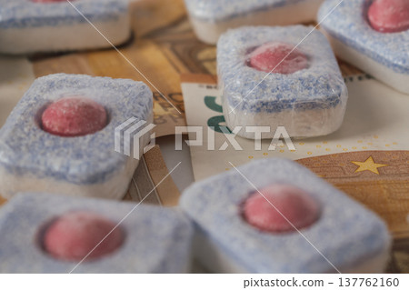 Dishwasher detergent tablets lying on euro currency banknotes against a white background Dishwasher detergent tablets lying on euro currency banknotes against a white background 137762160