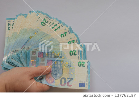 Female hand holding a large fan of 20 Euro banknotes against a white background. Vivid blue currency concept with extensive copy space for financial or business text Female hand holding a large fan of 20 Euro banknotes against a white background. Vivid blue currency concept with extensive copy space for financial or business text 137762187