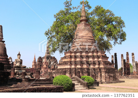 Ancient stone stupa and Buddha statue, Wat Mahathat, Sukhothai historical park. Picturesque scene with old stupa, Sukhothai old city, Northern Thailand. Topic of vacation, travel, trip, cruise, tour Ancient stone stupa and Buddha statue, Wat Mahathat, Sukhothai historical park. Picturesque scene with old stupa, Sukhothai old city, Northern Thailand. Topic of vacation, travel, trip, cruise, tour 137762351