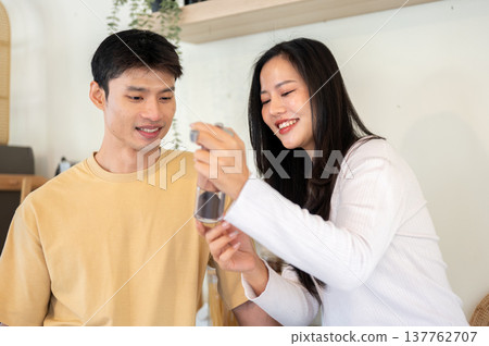 Asian woman girlfriend showing powder in grinder to a man boyfriend while making coffee in kitchen. Asian woman girlfriend showing powder in grinder to a man boyfriend while making coffee in kitchen. 137762707