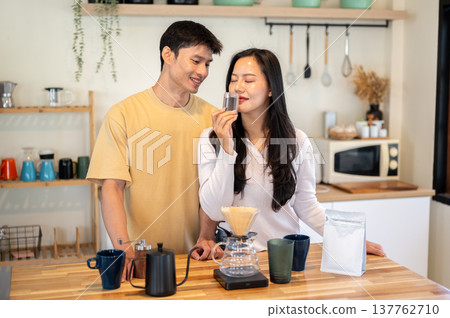 Asian couple a man looking at woman smelling powder aroma in grinder while making coffee in kitchen. Asian couple a man looking at woman smelling powder aroma in grinder while making coffee in kitchen. 137762710