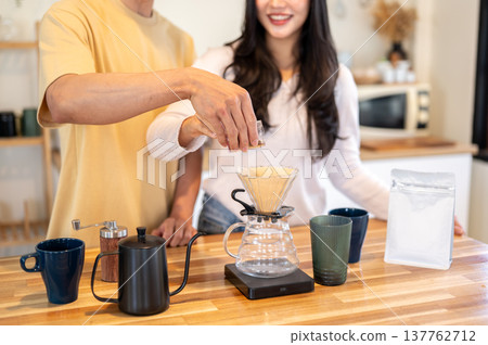 Close up of a man holding woman's hand pouring powder in dripper making coffee. Couple in kitchen. Close up of a man holding woman's hand pouring powder in dripper making coffee. Couple in kitchen. 137762712