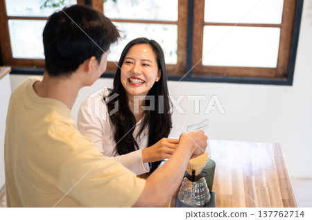 Asian man holding woman's hand pouring powder in dripper while making coffee. Couple in the kitchen. Asian man holding woman's hand pouring powder in dripper while making coffee. Couple in the kitchen. 137762714