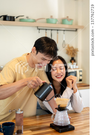 Pretty asian woman looking at man holding kettle pouring water making drip coffee on kitchen counter Pretty asian woman looking at man holding kettle pouring water making drip coffee on kitchen counter 137762719