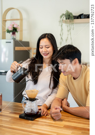 Asian man looking at woman holding kettle pouring water in dripper making coffee at kitchen counter. 137762723