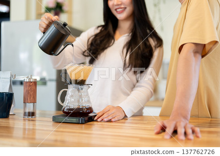 Close up man standing with woman holding kettle pouring water making drip coffee at kitchen counter. Close up man standing with woman holding kettle pouring water making drip coffee at kitchen counter. 137762726