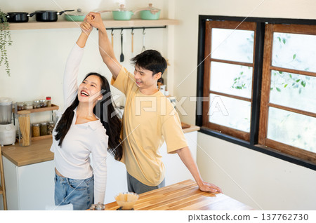Smiling asian man and woman couple holding hands dancing or spinning aside kitchen cooking counter. 137762730