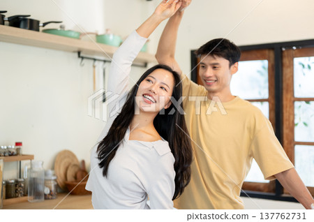 Pretty asian woman and a man couple holding hands dancing or spinning aside kitchen cooking counter. Pretty asian woman and a man couple holding hands dancing or spinning aside kitchen cooking counter. 137762731