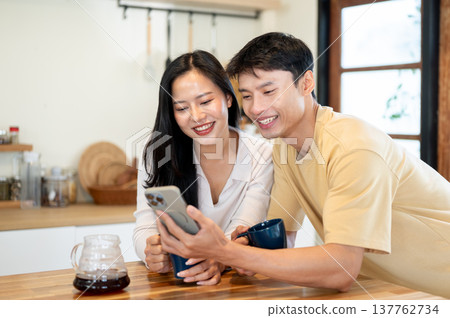 Pretty asian woman and man couple looking at phone watching videos making coffee at kitchen counter. 137762734