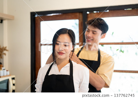 Asian couple a man tying woman or girlfriend's hair before cooking a food while standing in kitchen. Asian couple a man tying woman or girlfriend's hair before cooking a food while standing in kitchen. 137762745
