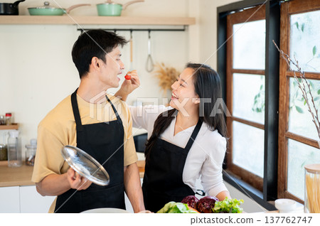 Asian couple woman feeding strawberry to boyfriend while cooking preparing food standing in kitchen. 137762747