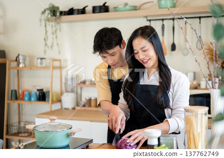 A man helping teaching woman girlfriend cooking food while standing at kitchen counter. Asian couple 137762749