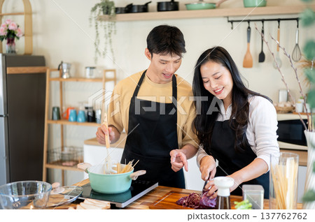 Asian couple a man boiling spaghetti and woman girlfriend cuts vegetable at kitchen cooking counter. Asian couple a man boiling spaghetti and woman girlfriend cuts vegetable at kitchen cooking counter. 137762762