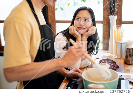 Pretty asian woman girlfriend smiling looking at a man boiling spaghetti at kitchen cooking counter. Pretty asian woman girlfriend smiling looking at a man boiling spaghetti at kitchen cooking counter. 137762766