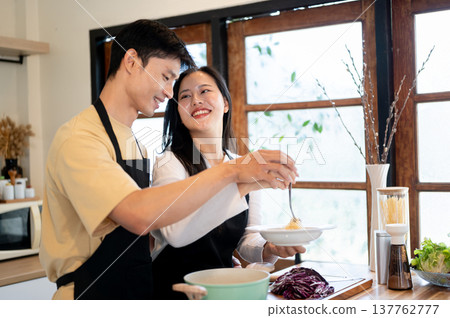 Asian couple holding hands over food plate woman girlfriend smiling at boyfriend at kitchen counter. Asian couple holding hands over food plate woman girlfriend smiling at boyfriend at kitchen counter. 137762777