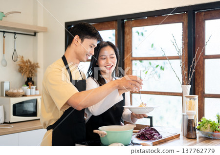 Asian couple a man boyfriend holding a woman girlfriend's hand over food plate at kitchen counter. Asian couple a man boyfriend holding a woman girlfriend's hand over food plate at kitchen counter. 137762779