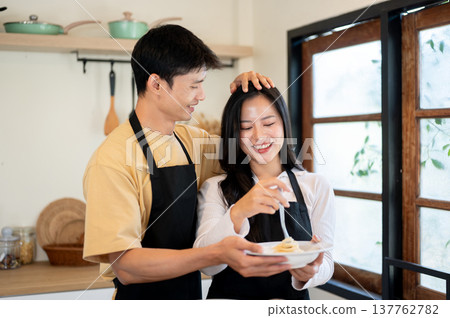 Asian couple man boyfriend patting head of woman girlfriend while cooking eating at kitchen counter. Asian couple man boyfriend patting head of woman girlfriend while cooking eating at kitchen counter. 137762782