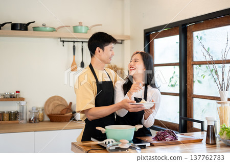 Asian couple man boyfriend giving woman girlfriend head pat while cooking eating at kitchen counter. Asian couple man boyfriend giving woman girlfriend head pat while cooking eating at kitchen counter. 137762783