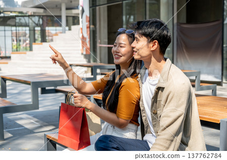 Asian couple man boyfriend with woman girlfriend holding shopping bag sitting at table outside mall. Asian couple man boyfriend with woman girlfriend holding shopping bag sitting at table outside mall. 137762784