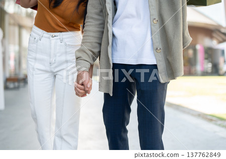 Close up of a stylish man and woman couple holding hands while standing walking together on sidewalk Close up of a stylish man and woman couple holding hands while standing walking together on sidewalk 137762849
