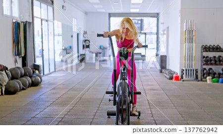 Woman intensely working out on air bike in gym Woman intensely working out on air bike in gym 137762942