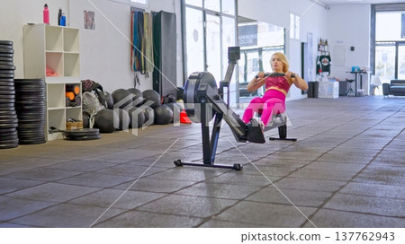 Woman training on rowing machine achieving fitness goals Woman training on rowing machine achieving fitness goals 137762943