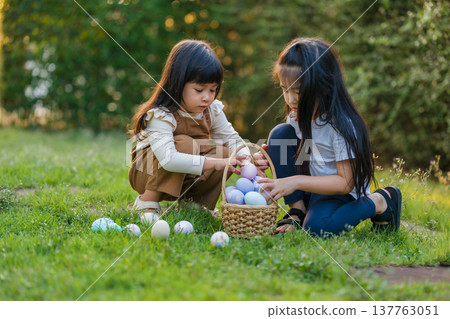 two child girl playing together and hunting for Easter eggs into basket on green grass in garden two child girl playing together and hunting for Easter eggs into basket on green grass in garden 137763051
