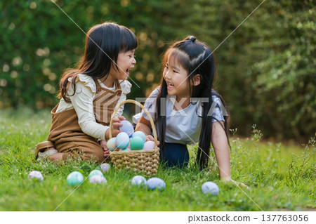 two happy child girl playing together and hunting for Easter eggs into basket on green grass in garden 137763056