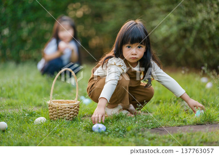 two child girl playing together and hunting for Easter eggs into basket on green grass in garden two child girl playing together and hunting for Easter eggs into basket on green grass in garden 137763057