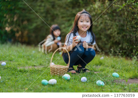 two happy child girl playing together and hunting for Easter eggs into basket on green grass in garden two happy child girl playing together and hunting for Easter eggs into basket on green grass in garden 137763059