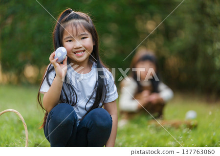 two happy child girl playing together and hunting for Easter eggs into basket on green grass in garden two happy child girl playing together and hunting for Easter eggs into basket on green grass in garden 137763060