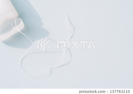 Dental floss strand from container on light blue background, minimal oral hygiene concept with copy space 137763210