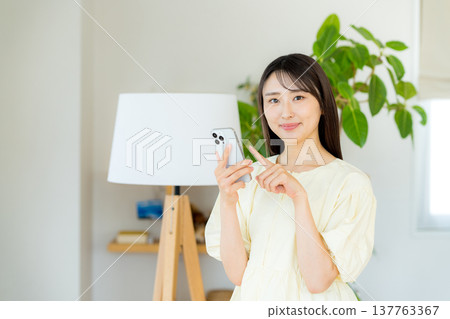 A woman who operates a smartphone in the room 137763367