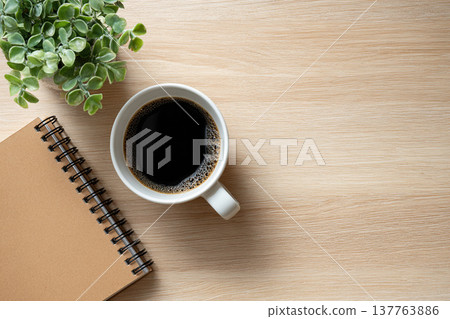 An overhead photo of a natural workspace with a coffee cup, a notebook, and a houseplant. 137763886