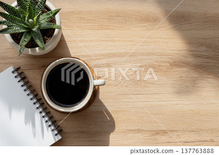 An overhead photo of a natural workspace with a coffee cup, a notebook, and a houseplant. 137763888