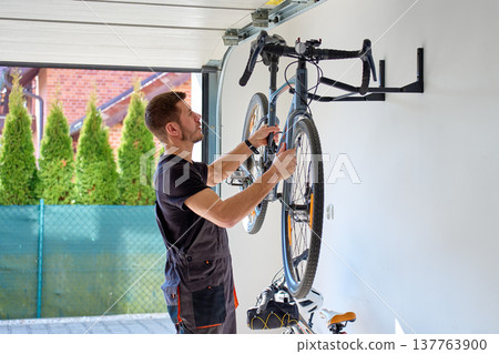 Man taking bicycle from wall rack for maintenance in garage 137763900