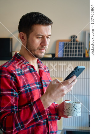 Man in pajamas drinking coffee and using smartphone at home Man in pajamas drinking coffee and using smartphone at home 137763904