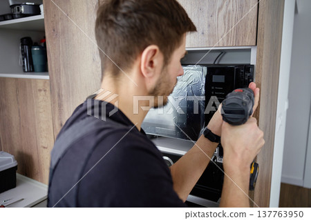 Man Using Power Drill to Fix Microwave Oven in Kitchen Cabinet Man Using Power Drill to Fix Microwave Oven in Kitchen Cabinet 137763950