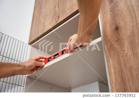 Hands using spirit level to align cabinet shelf during kitchen installation Hands using spirit level to align cabinet shelf during kitchen installation 137763952