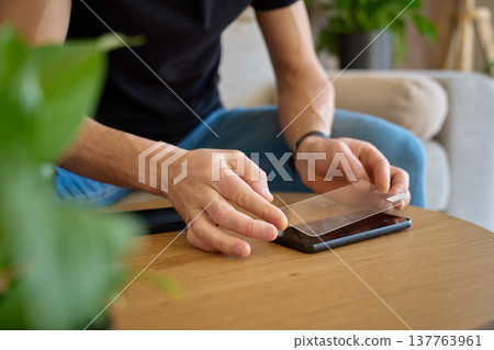 Man applying protective glass screen protector to smartphone at home Man applying protective glass screen protector to smartphone at home 137763961