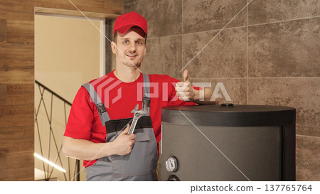 Smiling plumber showing thumbs up after successful heating system maintenance service in boiler room. Smiling plumber showing thumbs up after successful heating system maintenance service in boiler room. 137765764